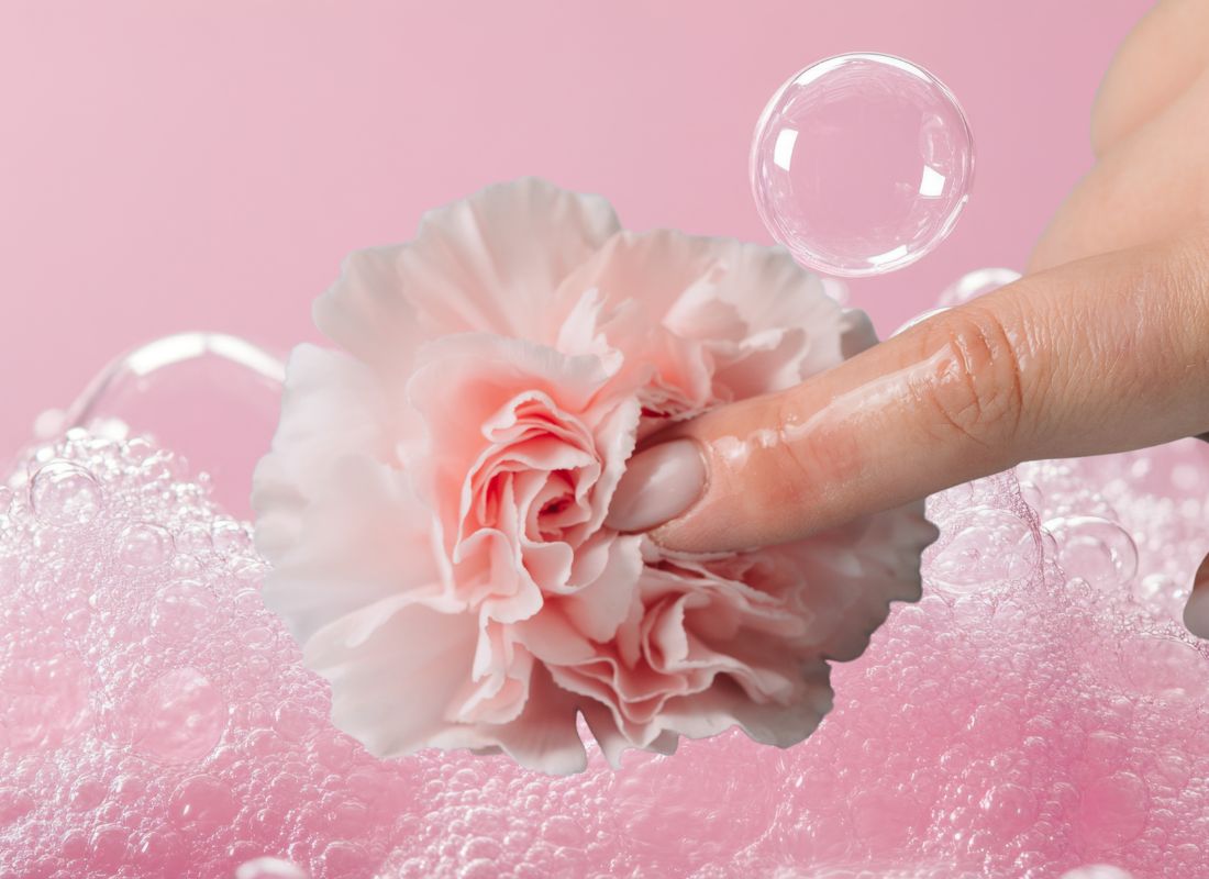 devojka prstom dodiruje cvet ruže, pozadina roze boje sa penom i mehurićima