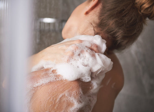 prikaz devojke pod tušem koja pere svoja leđa sa mrežicom za kupanje